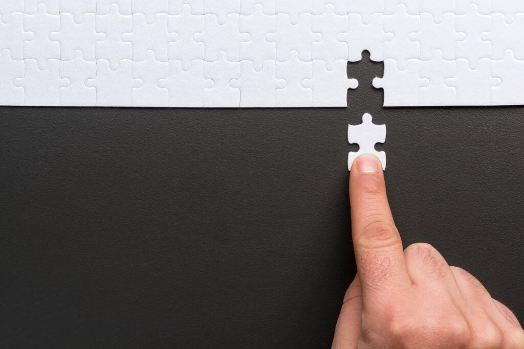 Person placing the last piece in a white jigsaw puzzle